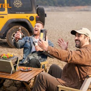 Hombre usando un smartphone resistente Oukitel para hacer una videollamada durante una acampada con barbacoa en el desierto.